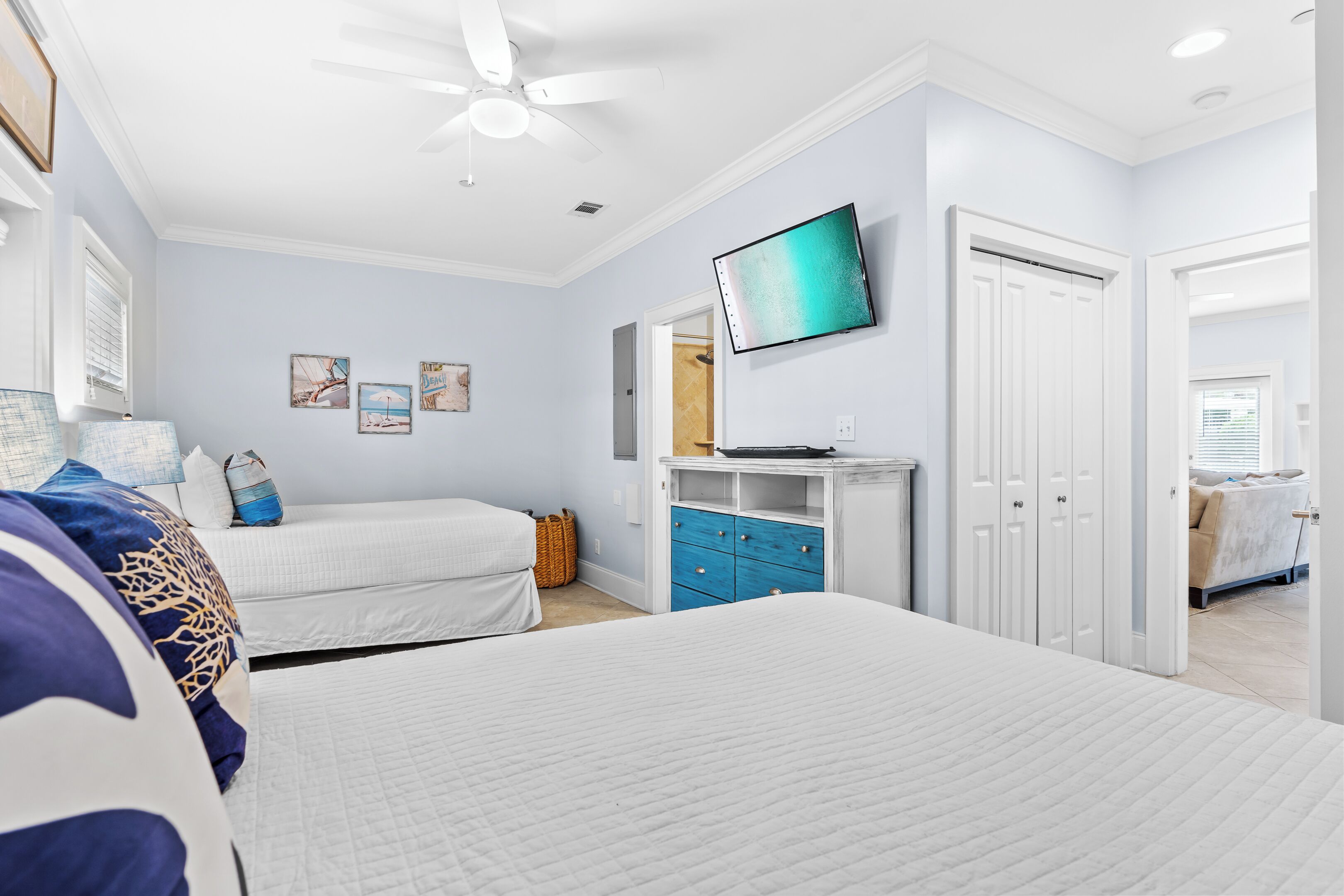 Une chambre avec deux lits, un ventilateur de plafond, une télévision, une commode et un placard.