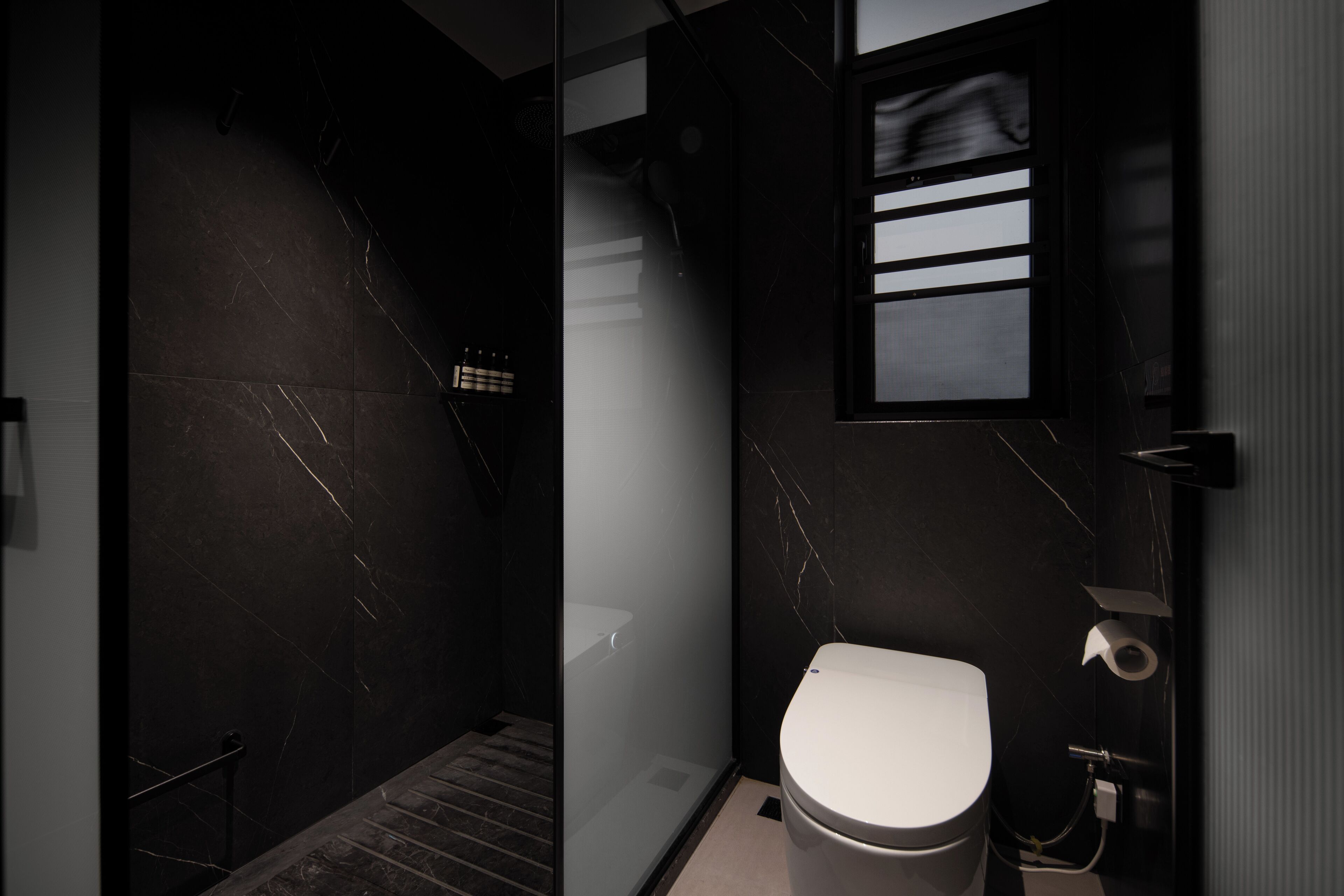 A modern bathroom with a glass-enclosed shower, a toilet, and a marble-tiled wall.