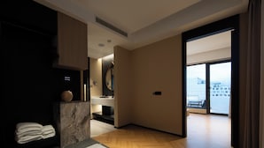 A modern hotel room with a marble accent wall, a wooden floor, a large window with a city view, and a bathroom with a sink and mirror. - See you soon at Ritz Rose Summer Hotel (Sanya)