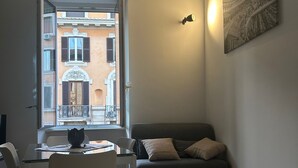 A cozy living room with a sofa, a dining table with chairs, and a view of a building through an open door. - Leonard Vatican House Deluxe  (Roma)