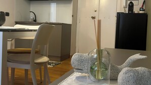 A modern kitchen with a white and gray color scheme, a dining area with a white table and chairs, and a decorative glass vase with reed sticks on the table. - Leonard Vatican House Deluxe  (Roma)