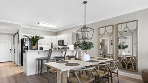 Une cuisine moderne avec des meubles blancs, un îlot central et un coin repas comprenant une table en bois et des chaises en osier.