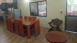 A dining area with a wooden table and chairs, a small round table, and a window with a metal gate. - Jovick Homestay (Siquijor)