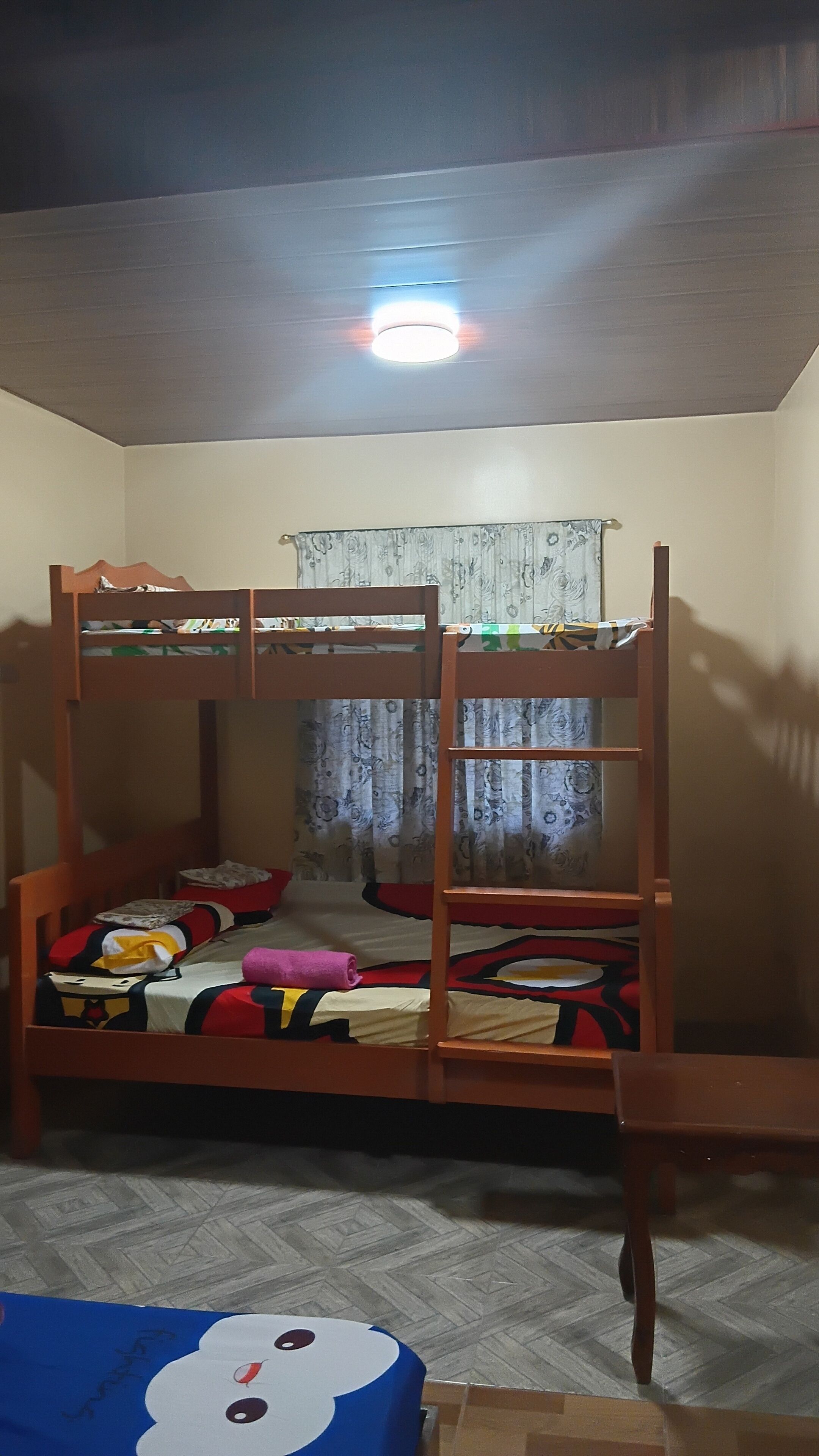 Dormitorio con literas, una lámpara en el techo, cortinas estampadas y piso con patrón de espiga.