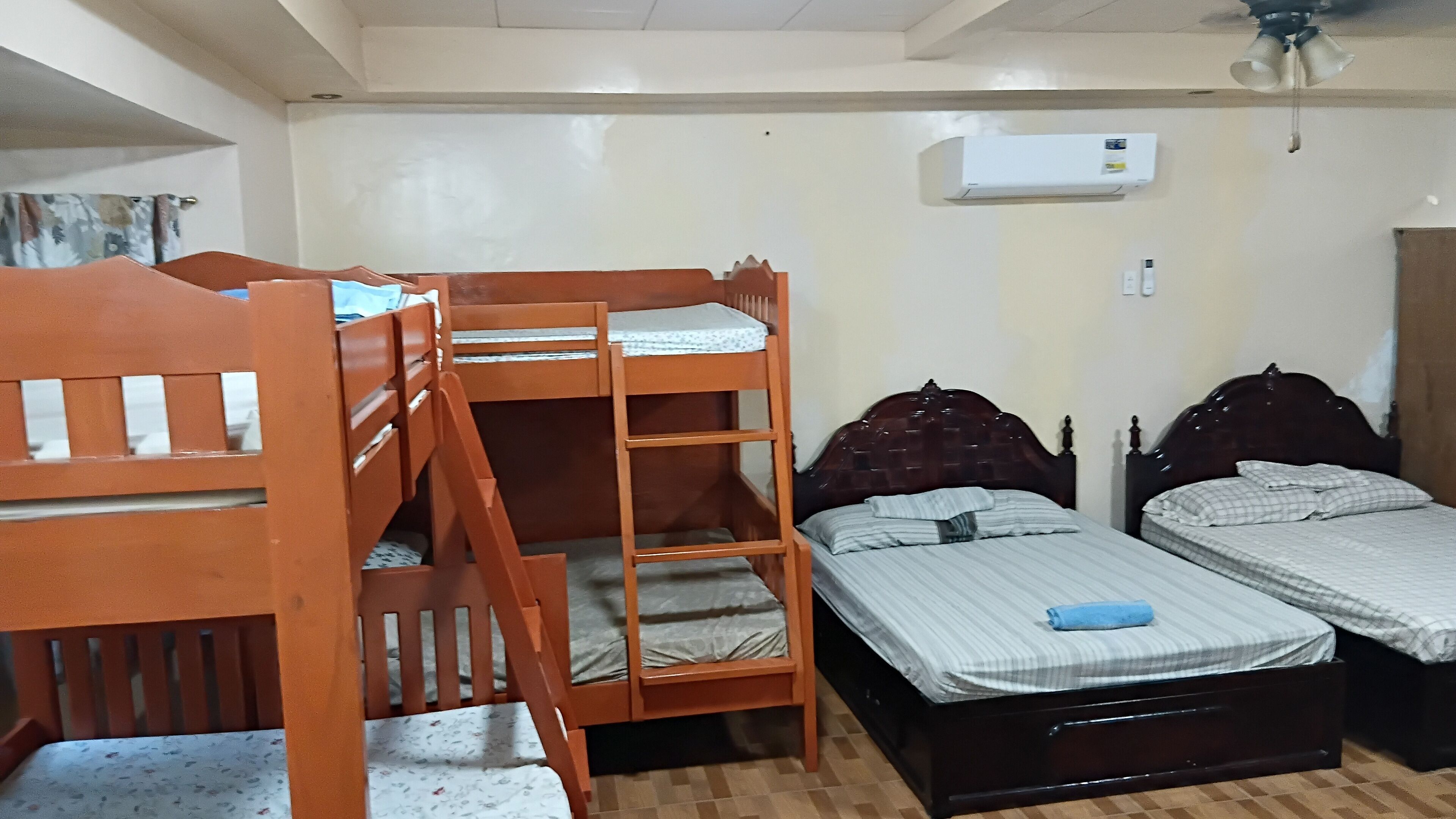 A room with bunk beds, a single bed, and an air conditioner on the wall.