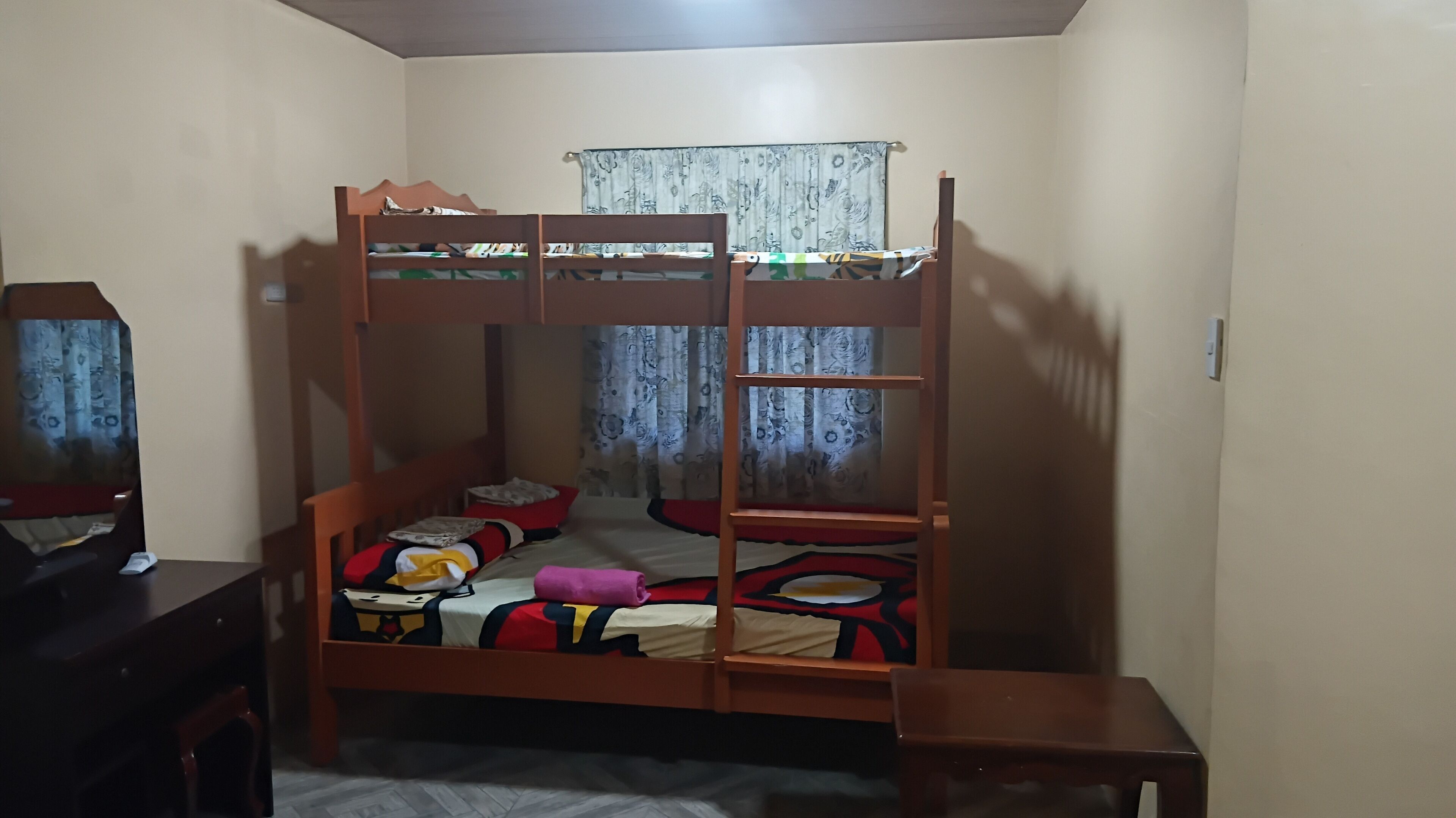 A bunk bed with a desk and chair, a window with curtains, and a wooden floor.