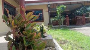 A house with a front yard, a small tree, and a concrete planter with plants. - Jovick Homestay (Siquijor)
