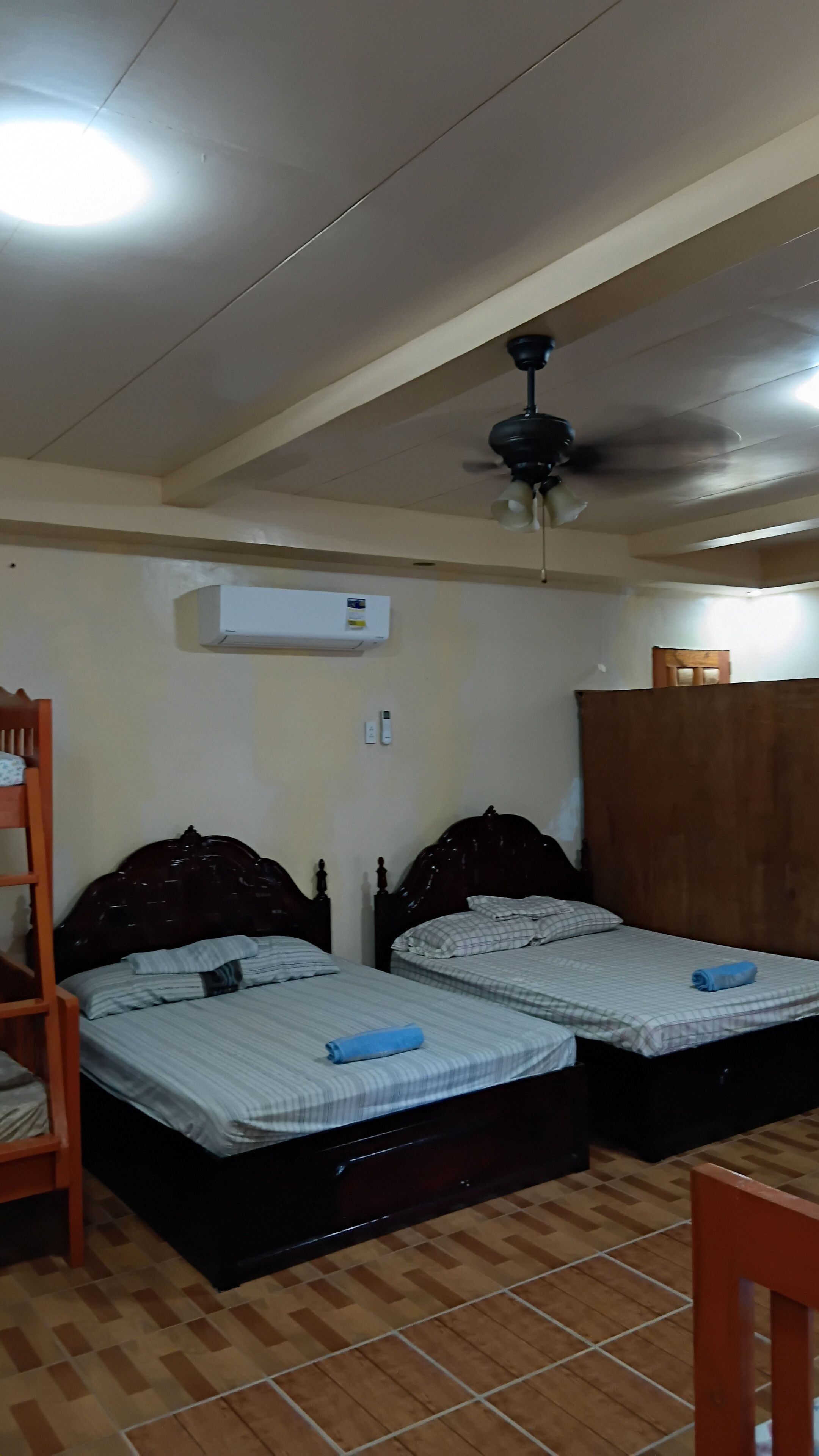 A room with two beds, a ceiling fan, an air conditioning unit, and a wooden floor.