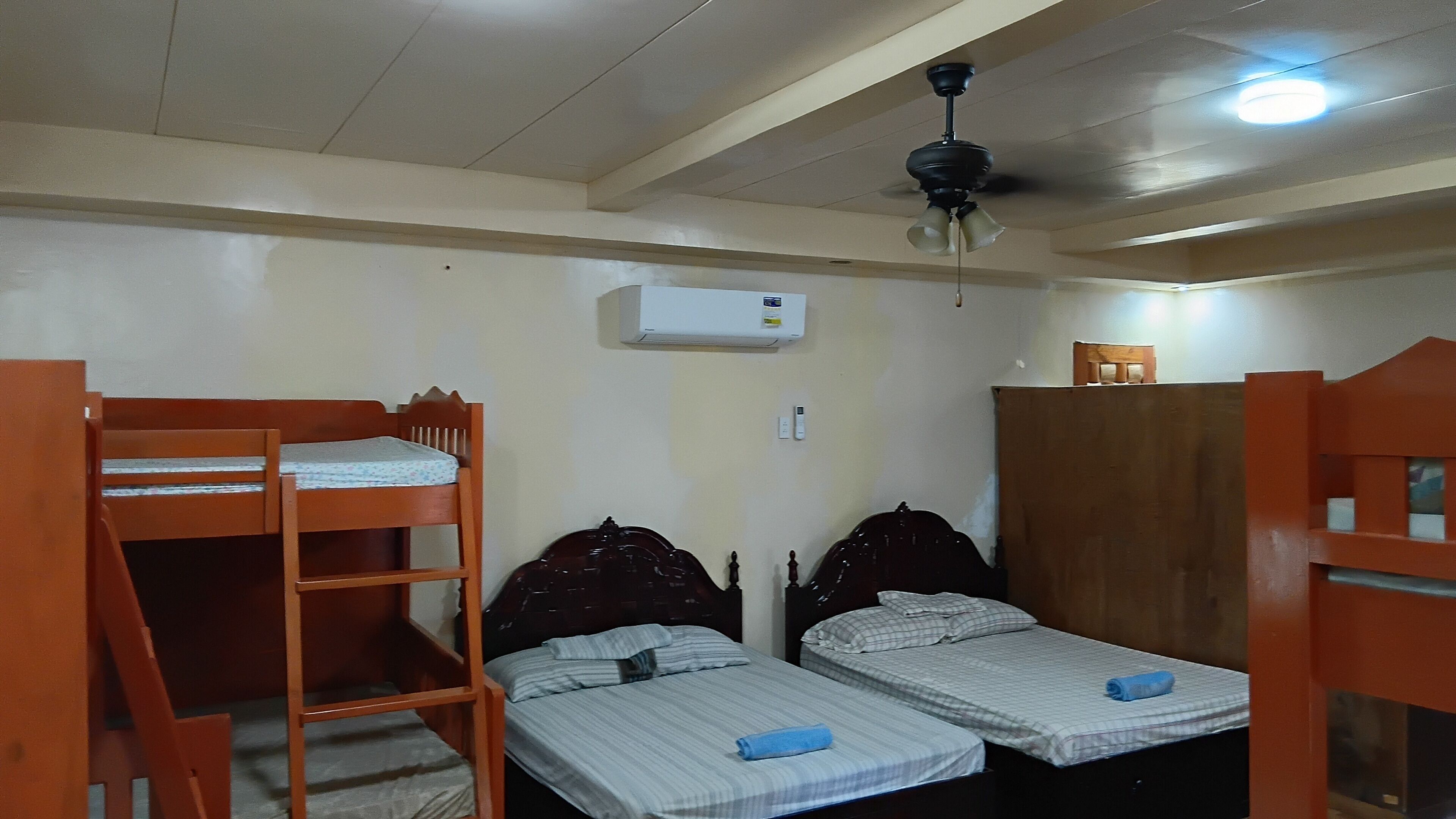 Une chambre de dortoir avec des lits superposés, un ventilateur de plafond, un appareil de climatisation et une armoire en bois.