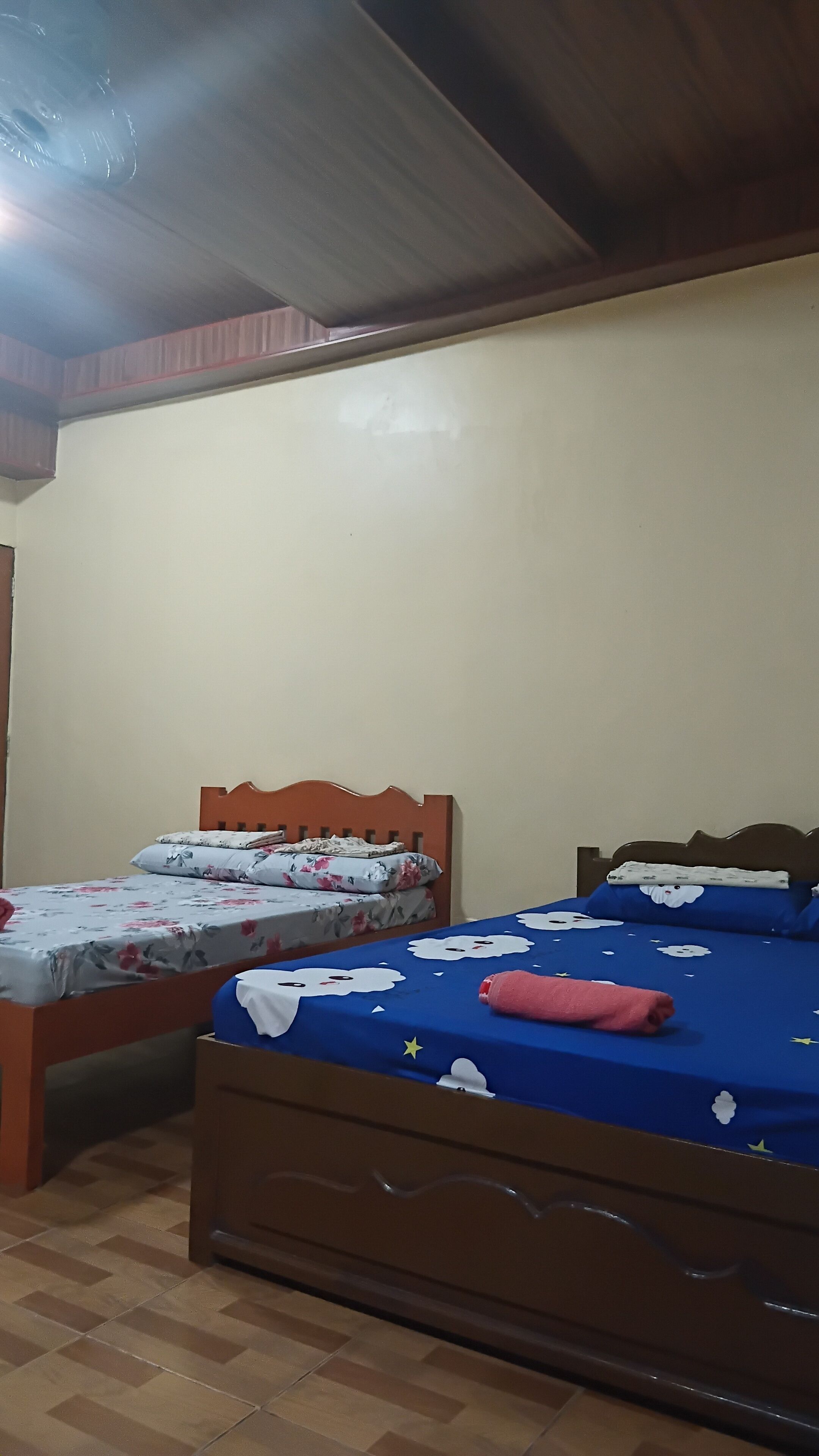 A bedroom with two beds, wooden headboards, and a tiled floor.