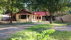 A two-story house with a red roof, a porch with chairs, and a small garden area. - Jovick Homestay (Siquijor)