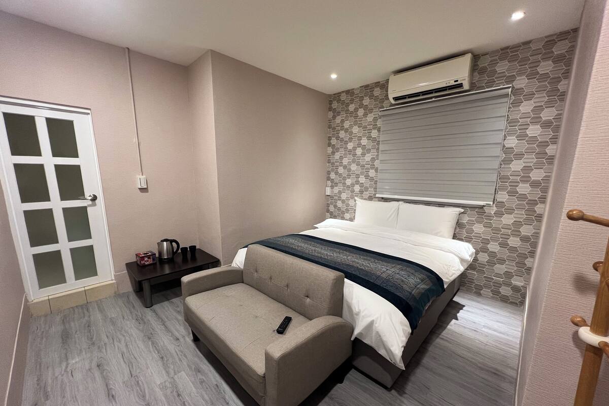 A bedroom with a bed, a bedside table, a chair, a wardrobe, and an air conditioning unit.