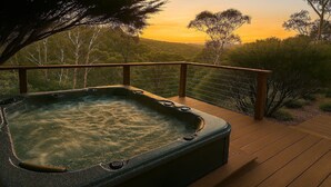 A hot tub on a wooden deck with a view of trees and hills.