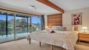 A bedroom with a large bed, a wooden headboard, a painting, and a view through a sliding glass door.