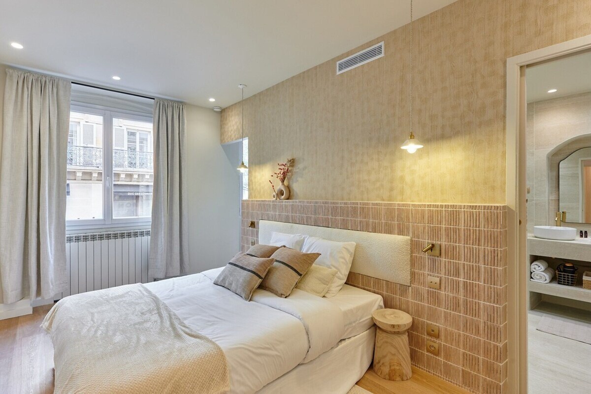 Ein Hotelzimmer mit Bett, einem runden Holfnachtisch, einem Spiegel und Blick ins Freie.