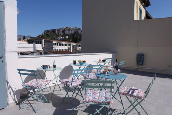 A terrace with blue metal chairs and tables, a view of a historic building, and a clear sky. - IPELHOME AVISSINIAS APARTMENTS (Athens)