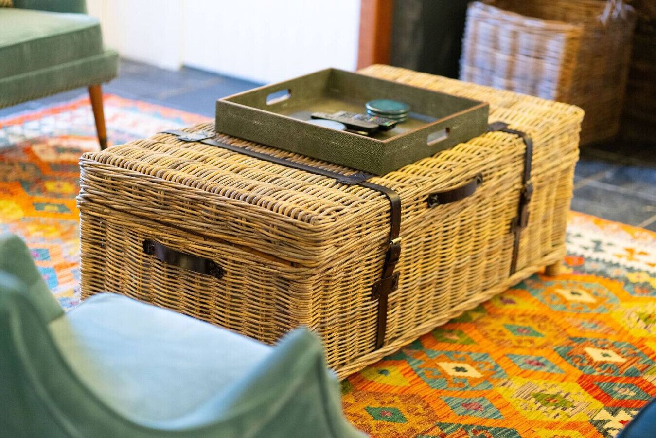 A wicker storage box with a metal tray on top, placed on a patterned rug.