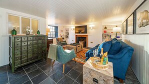 Een knusse woonkamer met een blauwe bank, een groene fauteuil en een houten kast.