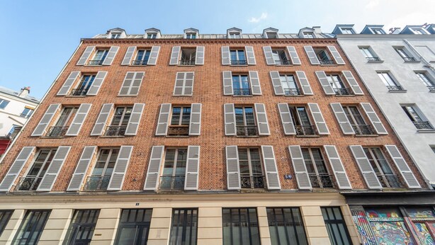 Um edifício de vários andares com fachada de tijolo, várias janelas com persianas e sacadas.