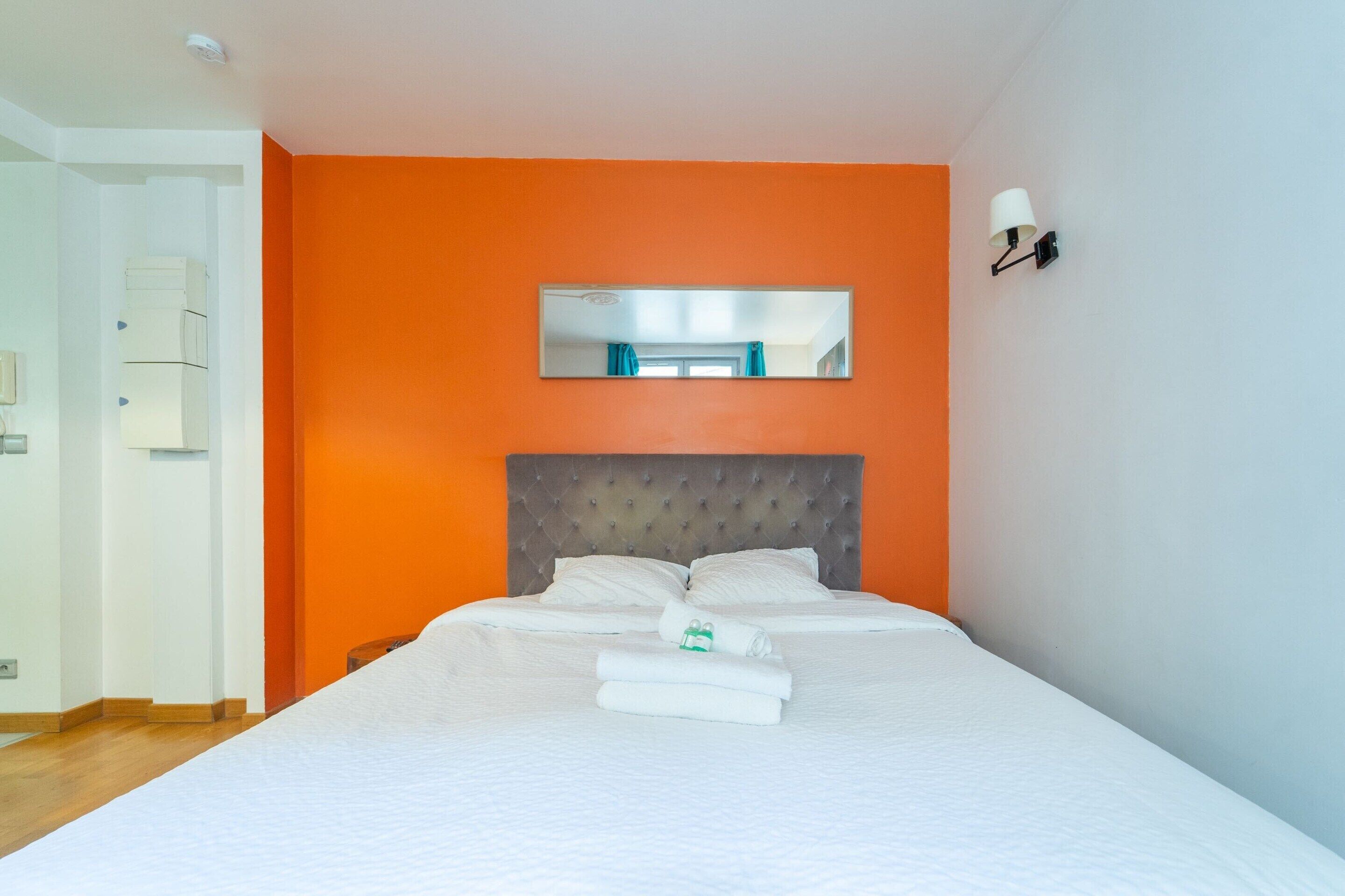 A hotel room with a bed, a headboard, a mirror, and a wall-mounted light fixture.