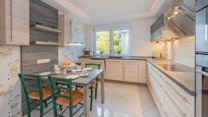 A modern kitchen with a dining area, featuring light wood cabinetry, a large window, and a built-in oven. - Villa Ost - Apartment Simone - high-quality designed domicile (Zinnowitz)