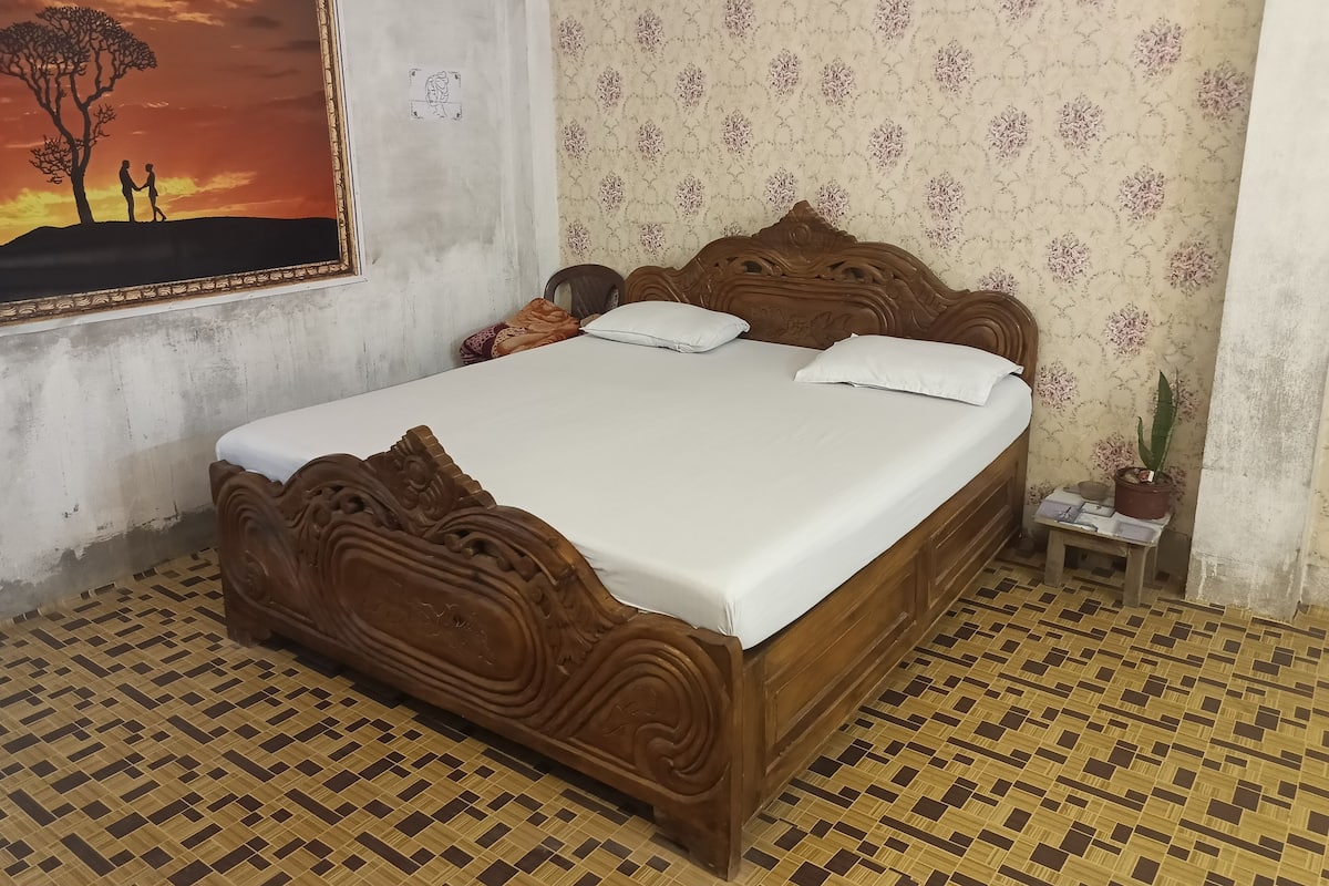 A bedroom with a wooden bed, a floral wallpaper, and a painting of a sunset.