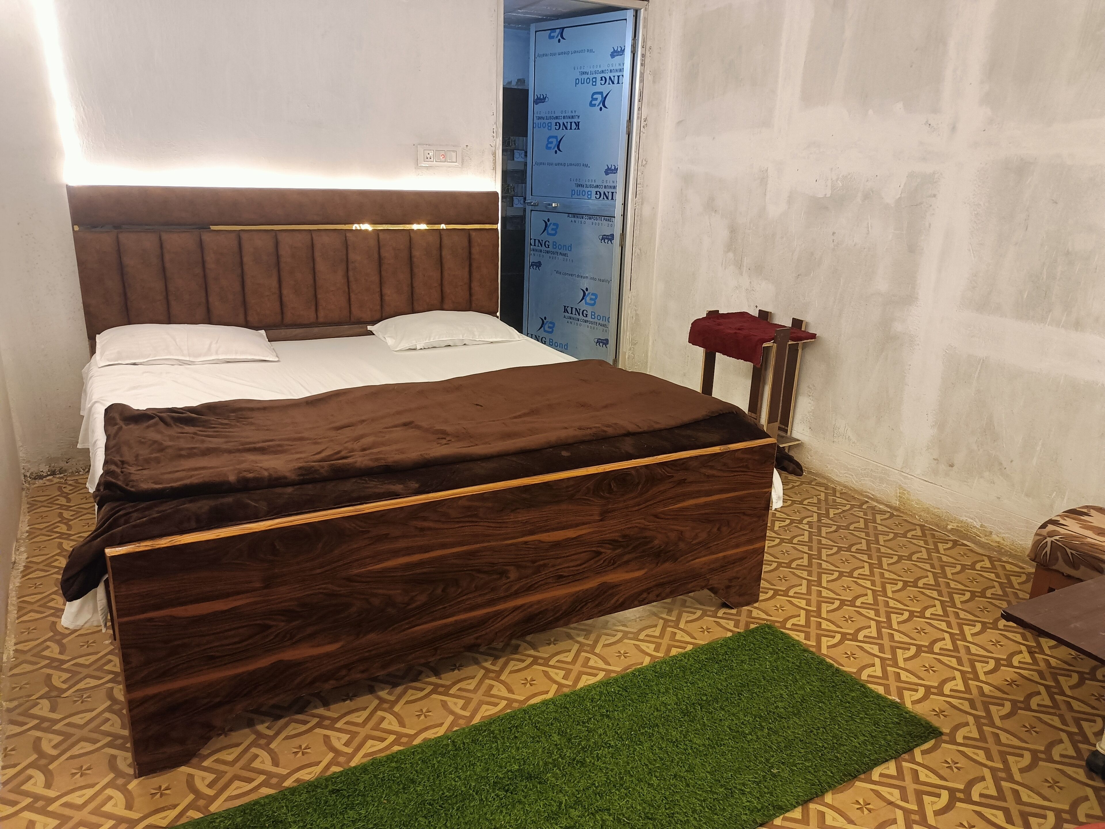 Un dormitorio con cama de madera, alfombra verde, baldosas de suelo estampadas y pared azul con aislamiento.