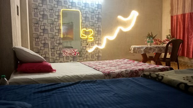 A bedroom with a bed, a small table with a tablecloth, a chair, and a wall with a geometric pattern. - Kalzug (Katihar)
