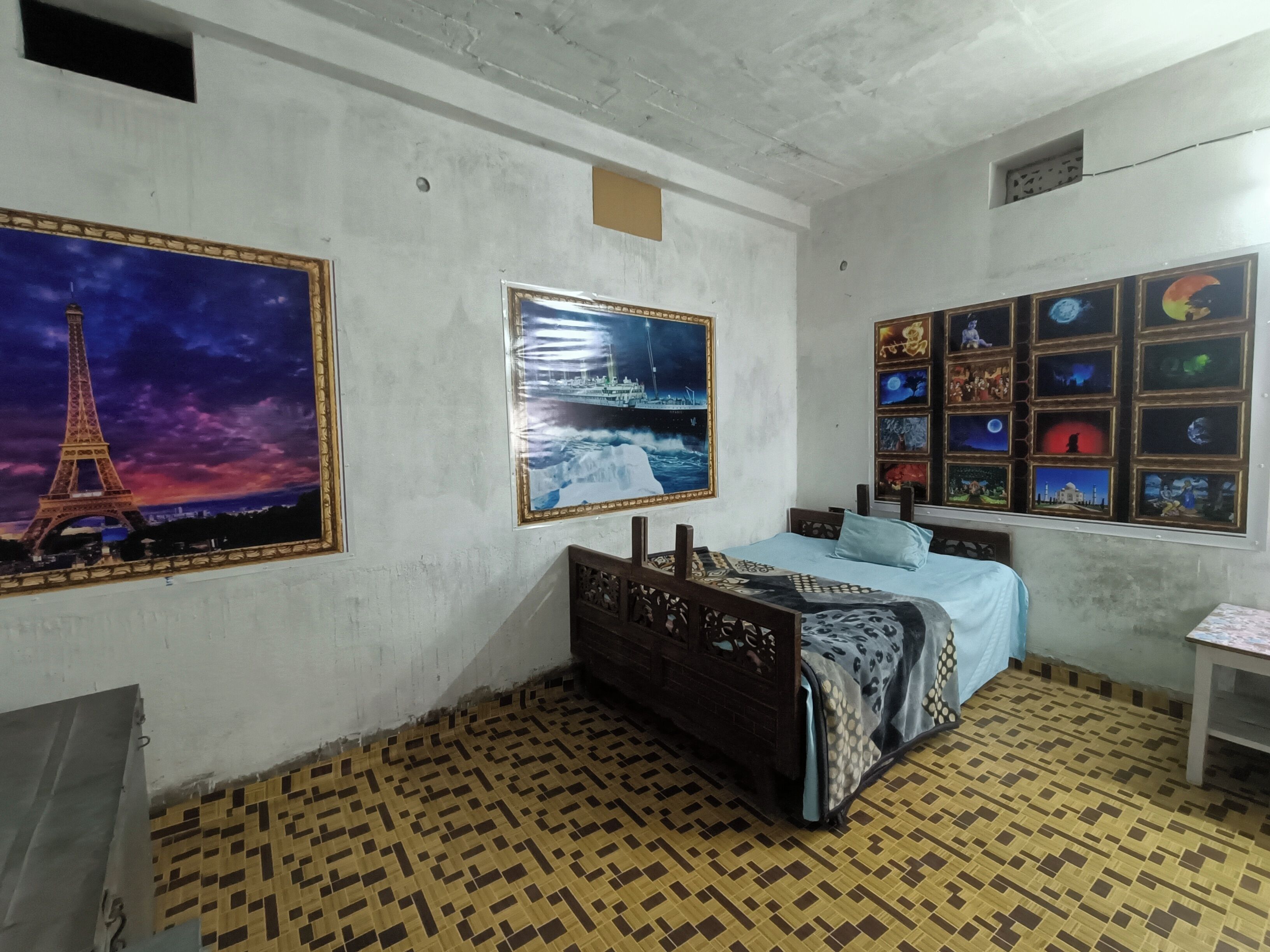 A bedroom with a bed, a wall with framed pictures, and a patterned floor.