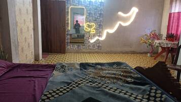 A room with a patterned floor, a bed with a patterned blanket, a mirror with a neon light, a table with a plant, and a wall with a geometric pattern.