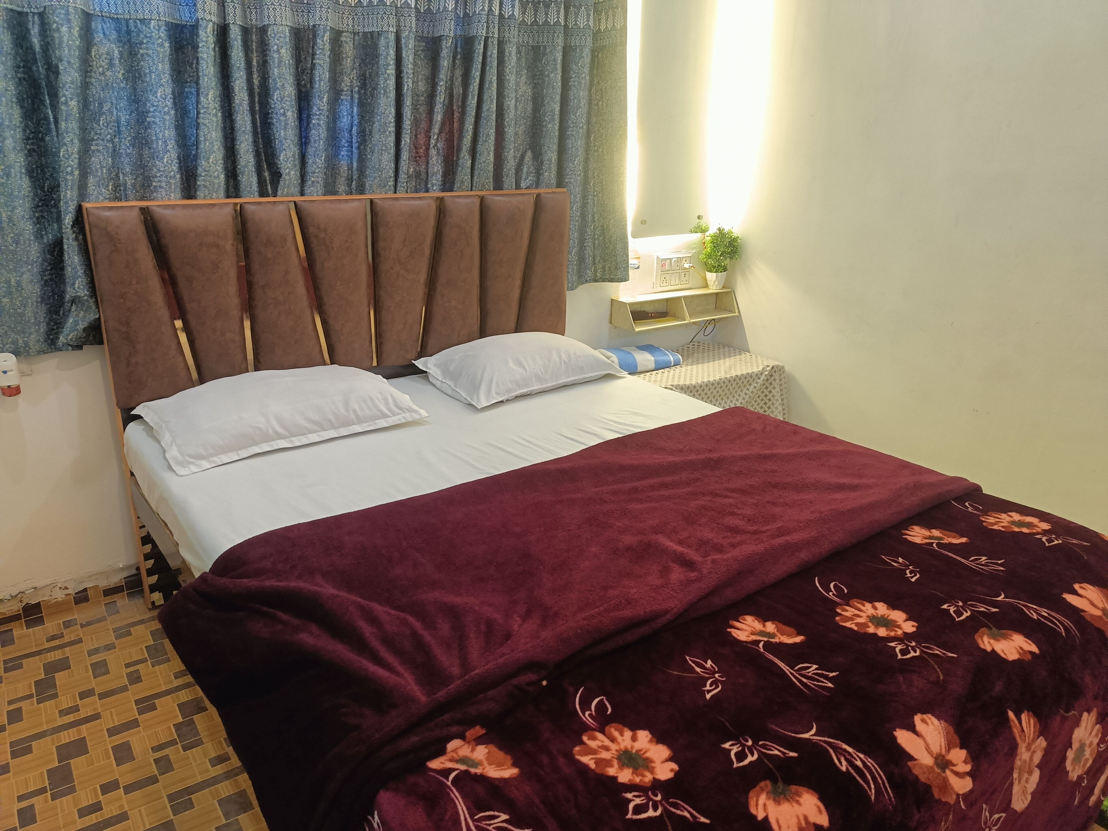 Una cama bien hecha con cabecera, ropa de cama blanca y una manta color burdeos con motivos florales.