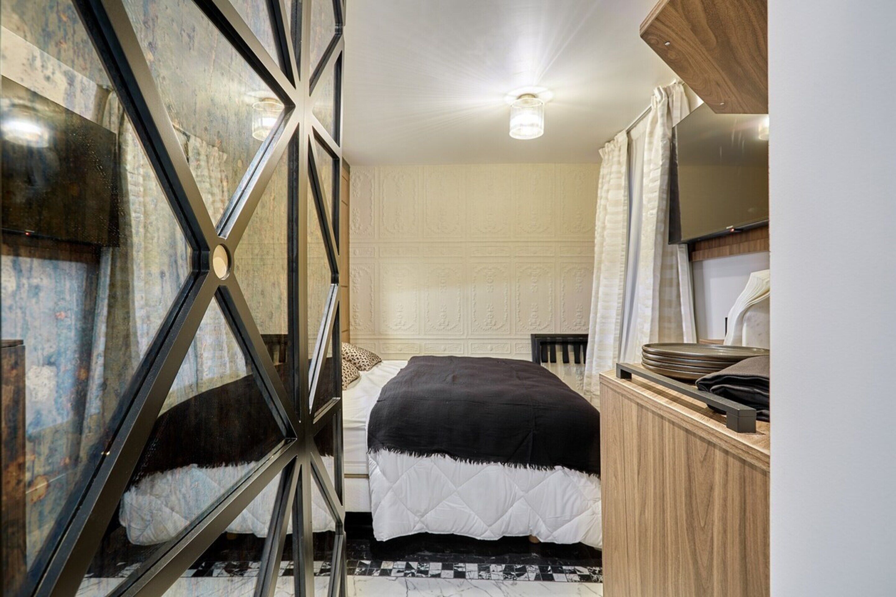 Un dormitorio con una cama, un armario de madera, una televisión y un papel tapiz estampado.