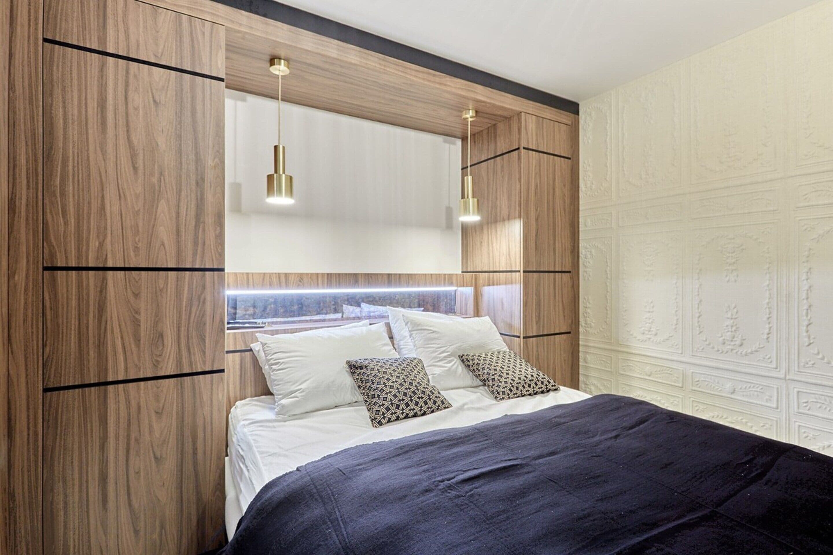 Een moderne slaapkamer met een groot bed, houten lambrisering en hanglampen.