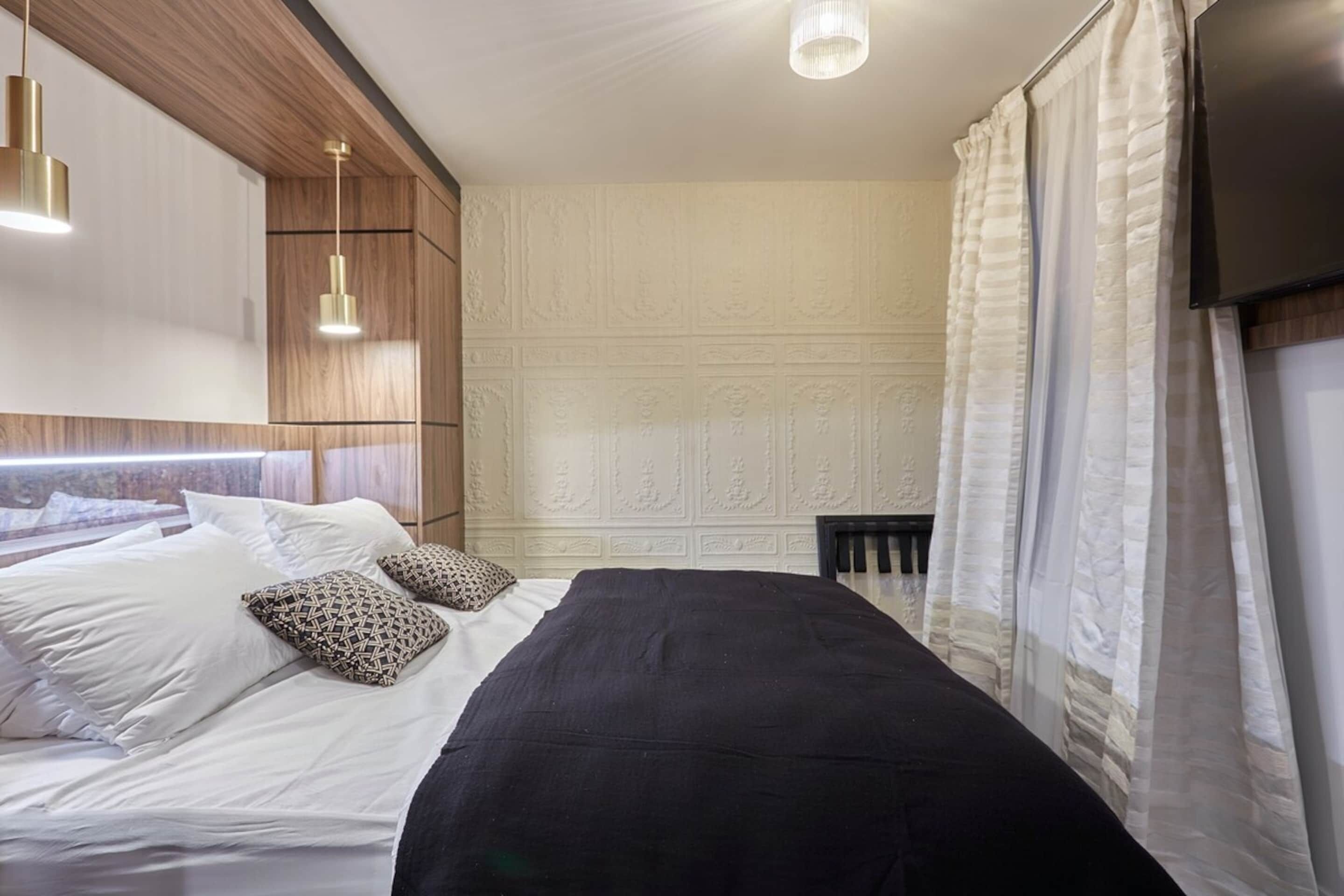 A bedroom with a bed, pillows, a headboard, a TV, and a ceiling light.