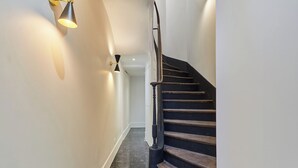 Eine moderne Treppe mit hölzernem Geländer und schwarzen Stufen, die zu einer Zwischenebene mit einer Lampe führt.