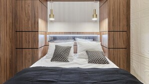 Ein Schlafzimmer mit einem hölzernen Kopfteil, zwei Nachttischlampen, gemusterten Kissen und einer schwarzen Bettdecke.