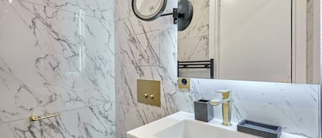 A modern bathroom with a white marble sink, gold faucet, and a wall-mounted mirror.