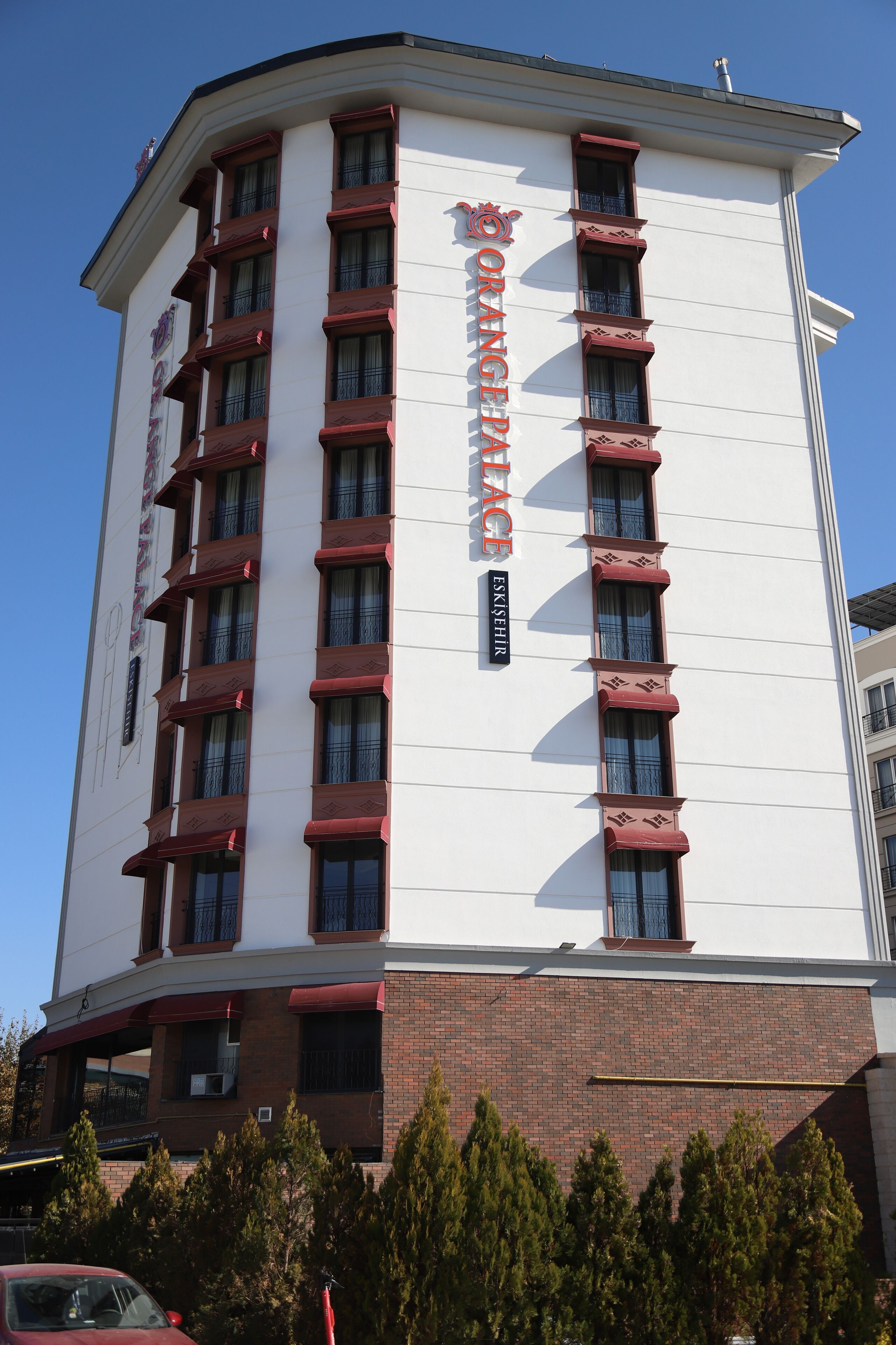 En høj hotelbygning med hvid facade og røde detaljer, med flere altaner og en klar himmel i baggrunden.