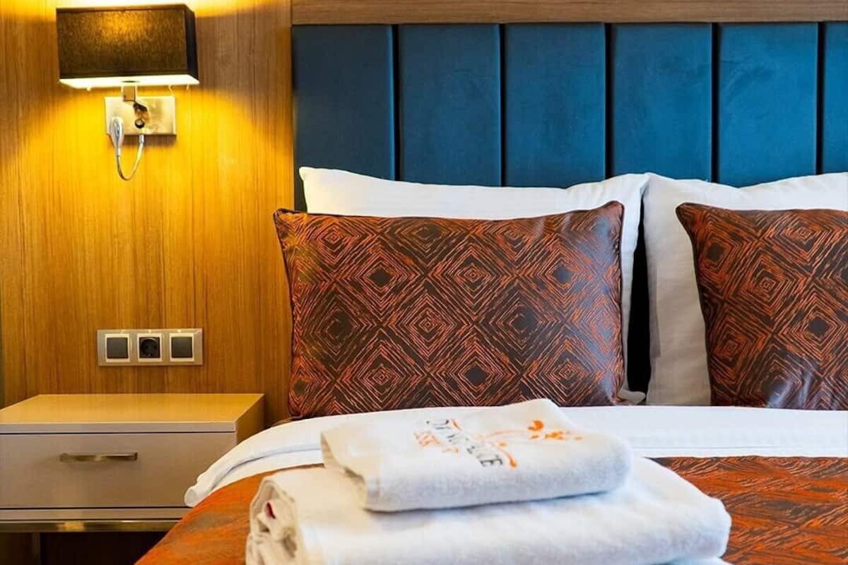 Una habitación de hotel con una cama, dos almohadas, una mesita de noche, una lámpara y una toalla doblada.