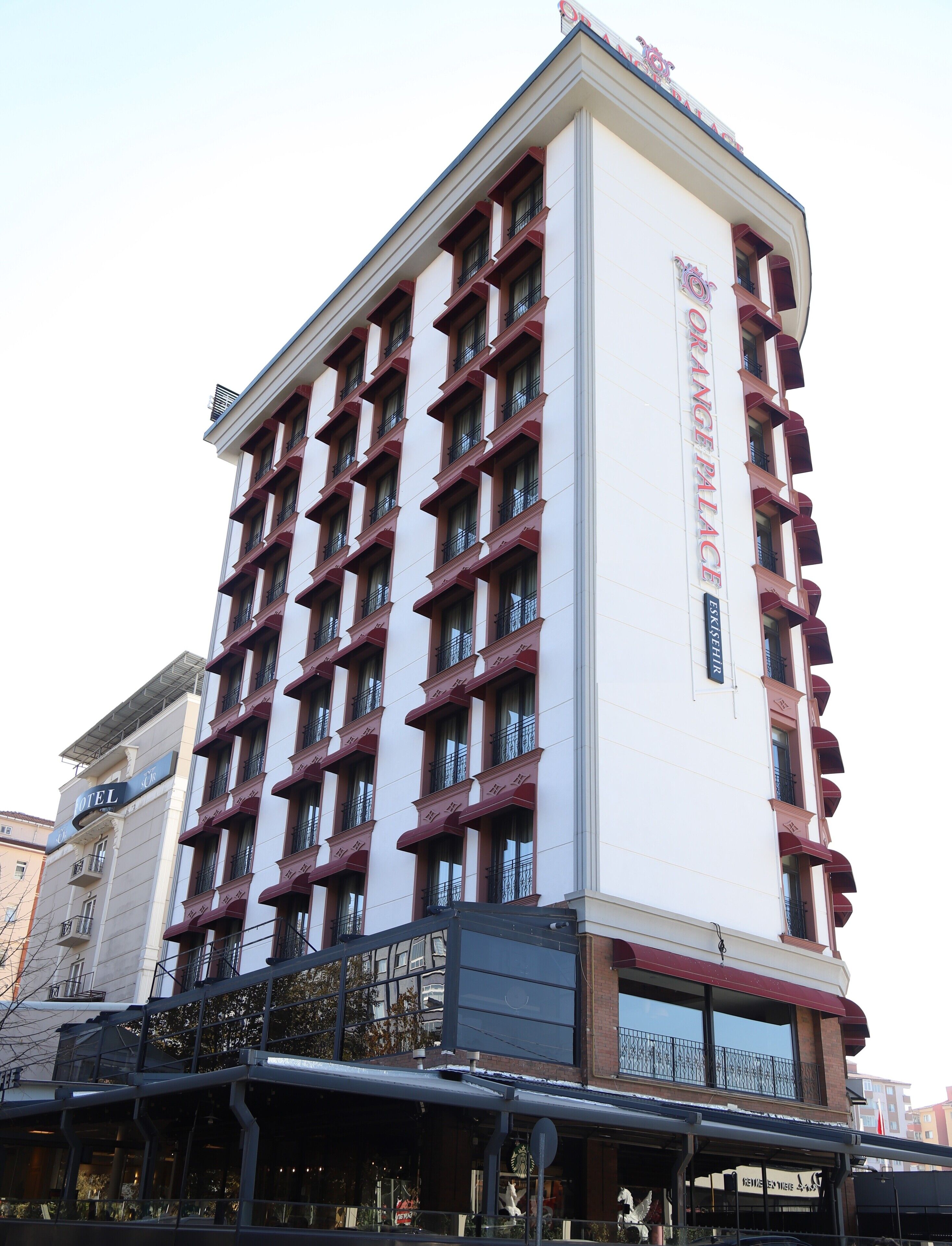 Ett hotell med flera våningar, en vit fasad och röda detaljer. Hotellet har en framträdande skylt med texten ”Hotel Orange Palace”.
