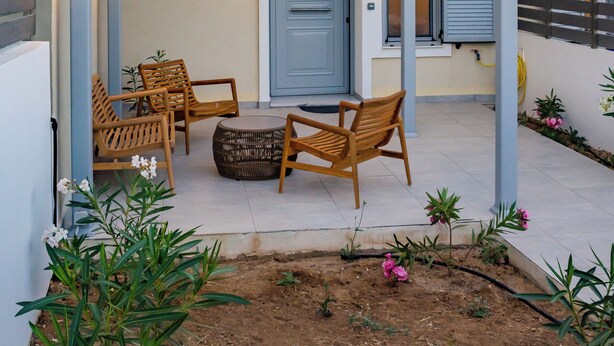 A covered outdoor seating area with wooden furniture and a door in the background. - Onyro Villas (Karpathos)