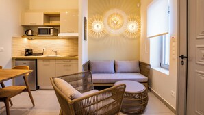 A compact kitchen with a microwave, toaster, and sink. There is a dining area with a wooden table and chairs. A wicker sofa and a small round table are also visible. - Onyro Villas (Karpathos)