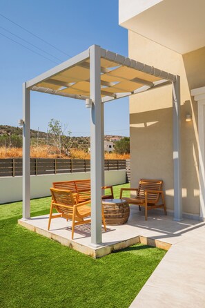 A covered patio with two wooden chairs and a woven basket. - Onyro Villas (Karpathos)