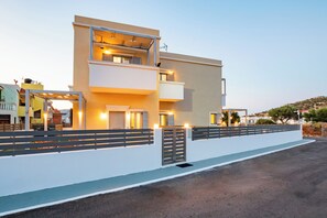 A modern multi-story building with balconies, a gated entrance, and a paved driveway. - Onyro Villas (Karpathos)