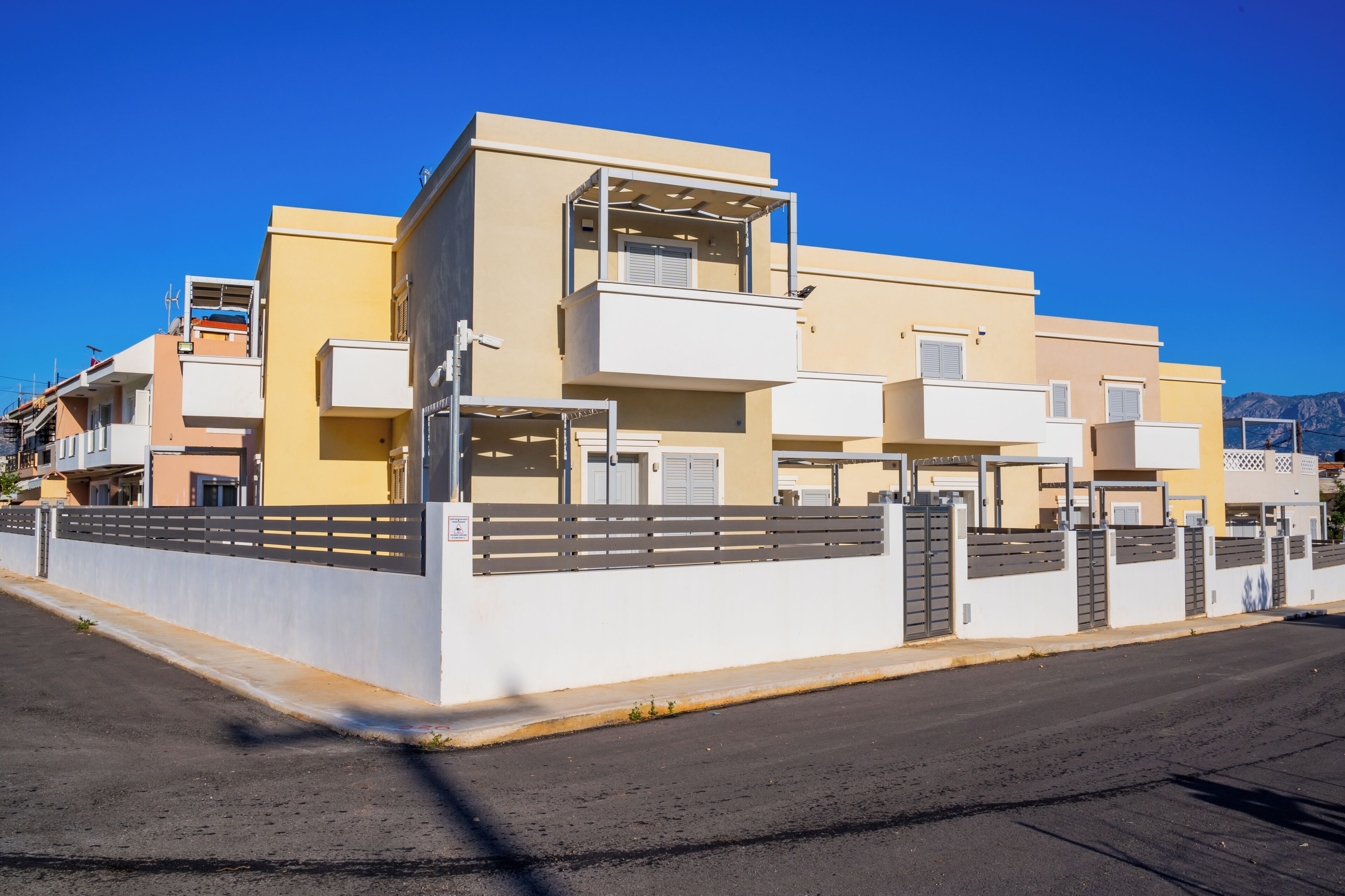 Un moderno edificio residencial con balcones, entrada protegida y cielo despejado.