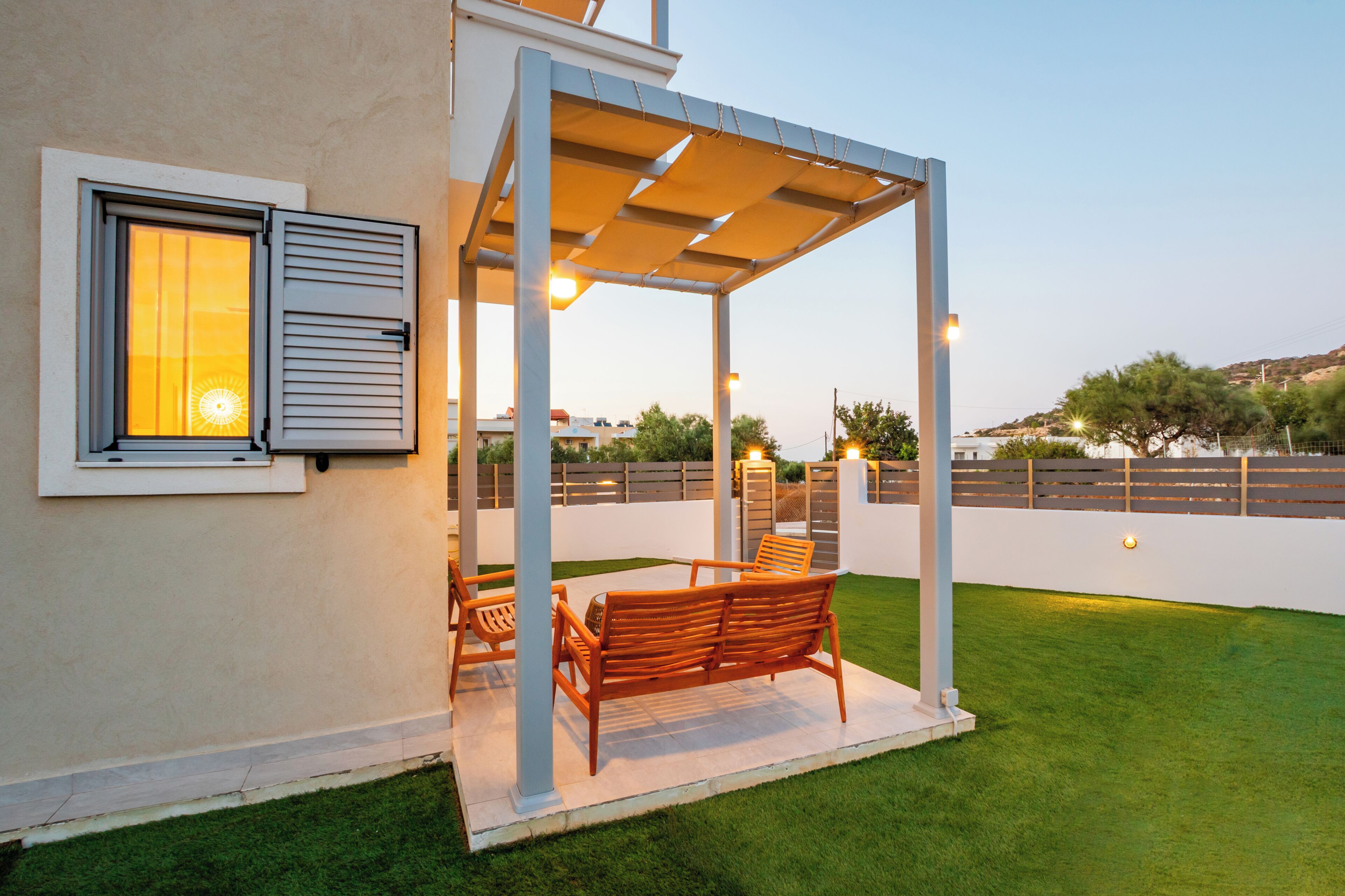 A covered outdoor seating area with a bench and chairs, a window with shutters, and a view of the surrounding landscape.
