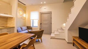 A modern living room with a wooden dining table, wicker furniture, a sofa, and a TV on a wooden stand. - Onyro Villas (Karpathos)