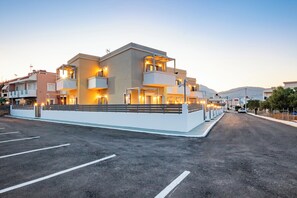 A modern multi-story hotel with balconies, a parking lot, and a clear view of the surrounding area. - Onyro Villas (Karpathos)