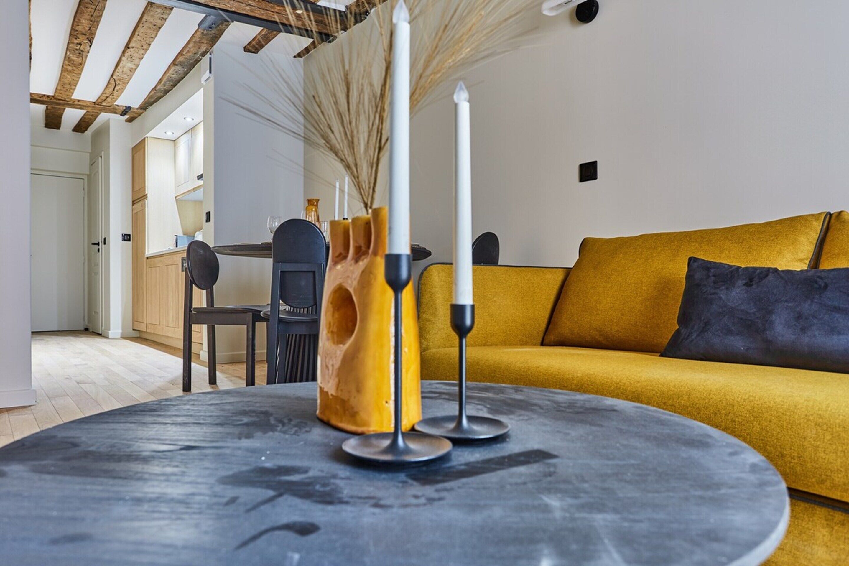 A modern living room with a round table, a sofa, and a kitchen in the background.