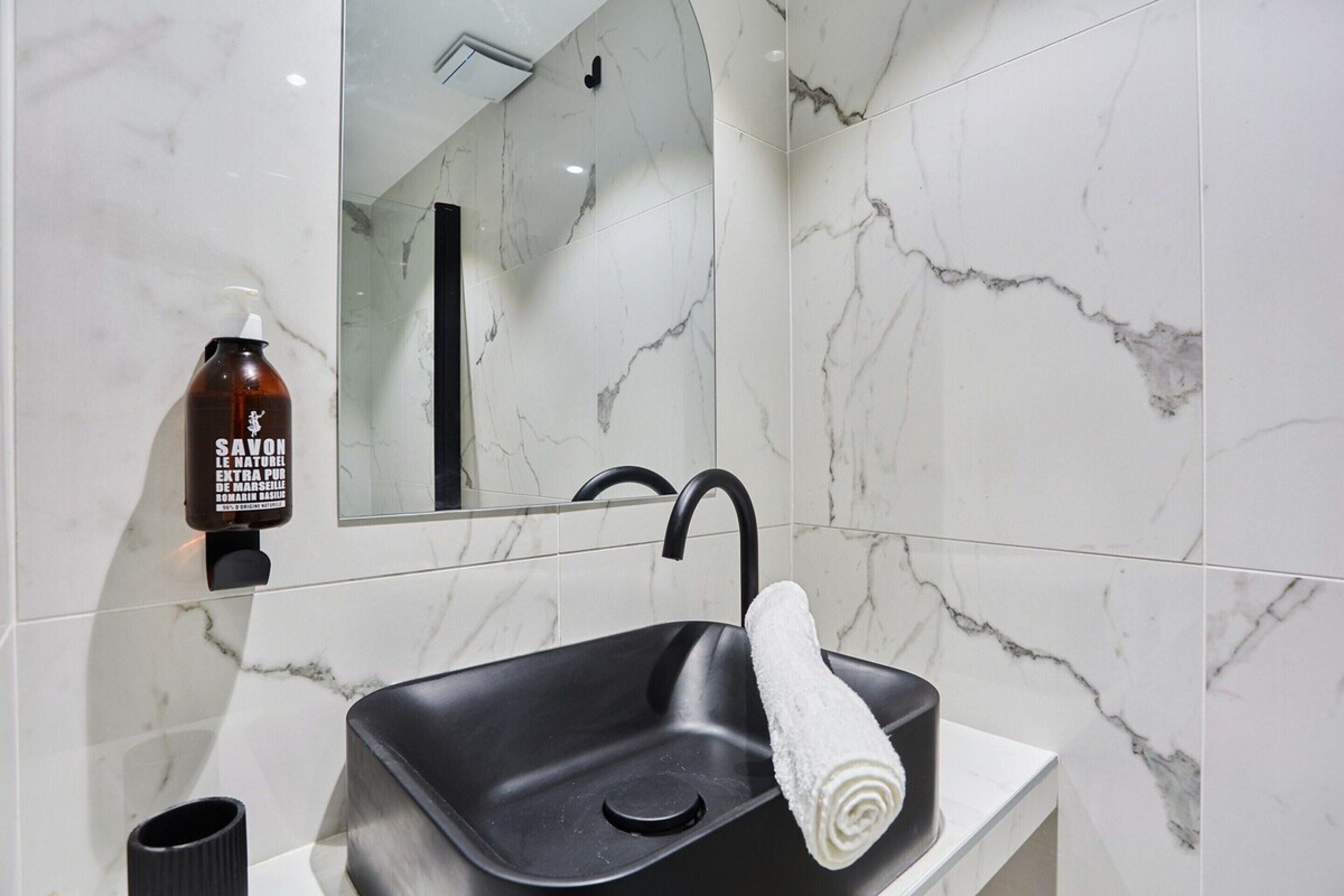 Une salle de bain avec un lavabo noir, un mur en marbre blanc et un miroir.
